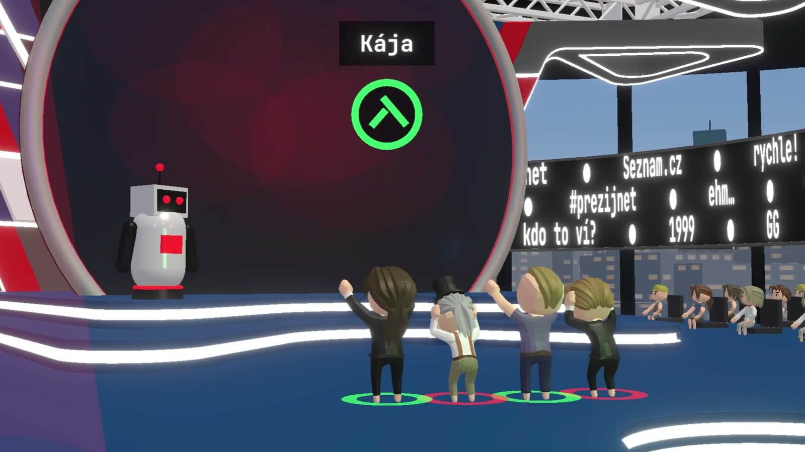 Druhé kruhové studio při odhalení výsledku: robotická moderátorka, slavící soutěžící a publikum po stranách pódia.